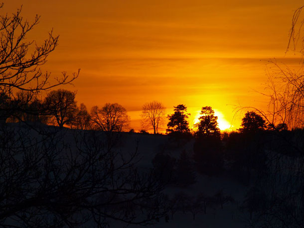 Sonnenaufgang und orangeroter Morgenhimmel über Hügeln und Bäumen von St. Johann, Schwäbische Alb