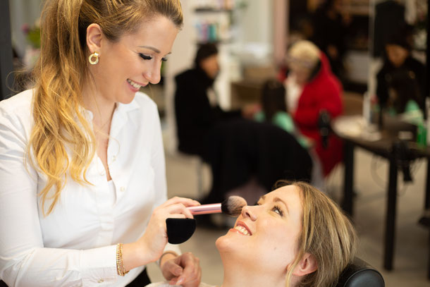 Zwei lachende Frauen die eine schminkt die andere für ein Braut Make Up