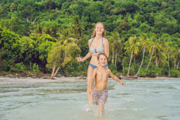 Eine Mutter und ihr Junge spielen lachend im flachen, warmen Meerwasser