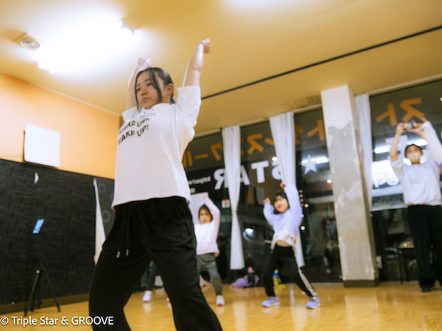 この画像は、新しくクラスを担当する講師のRIOがガールズダンスを子どもたちに熱心に指導している姿を表しています。