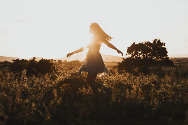 Frau tanzt auf Wiese mit Sonne im Hintergrund.