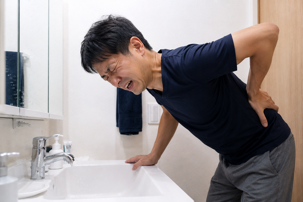 朝の洗顔中にぎっくり腰になり、痛みに耐えながら腰を支えている男性に画像です。