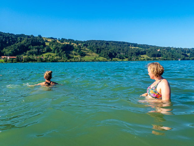Menschen mit und ohne Migrationsgeschichte genießen nach einer Wanderung eine Abkühlung im Großen Alpsee im Allgäu.