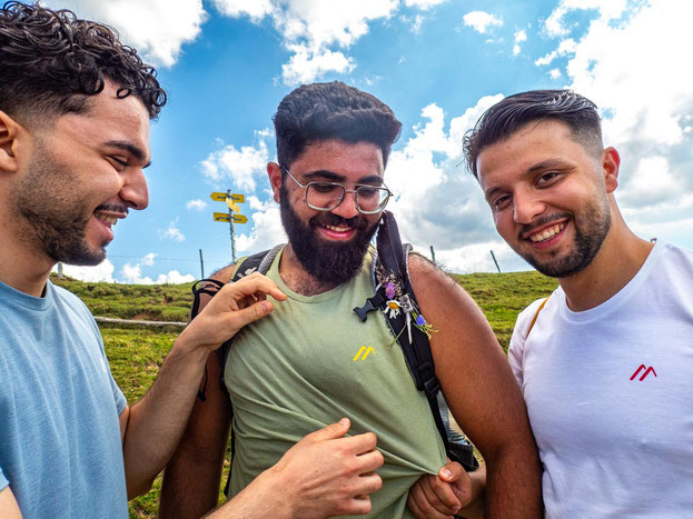 Drei Teilnehmende des Integrationsprojekts Wanderglück tragen T-Shirts von Maier Sports und lächeln sich im Allgäu an.