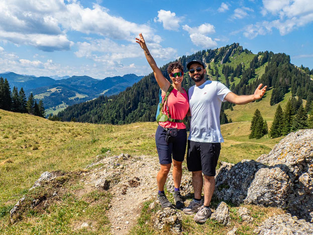 Zwei Teilnehmende des Integrationsprojekts Wanderglück stehen Arm in Arm vor der Bergkulisse der Nagelfluhkette im Allgäu und blicken gemeinsam in die Natur.