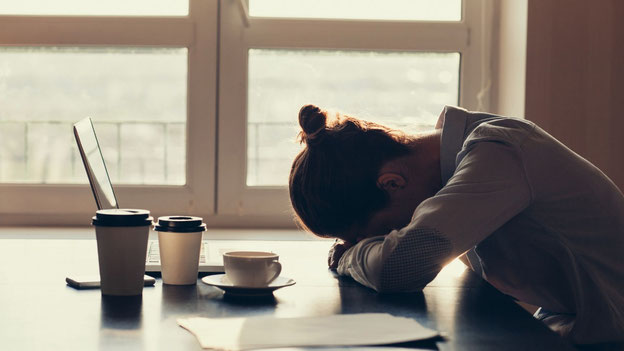 Femme brune épuisée qui dort devant son ordinateur. Il y a trois tasses de café sur la table.