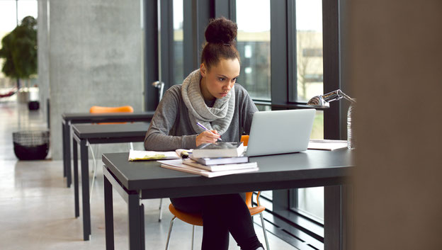 Studentin am Schreibtisch mit Laptop und Büchern