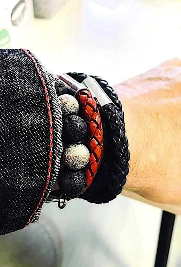 Am Handgelenk eines Mannes ein Mix aus einem schwarzen Lava Perlenarmband sowie eine, schwarzen Lederarmband und einem roten Lederarmband 