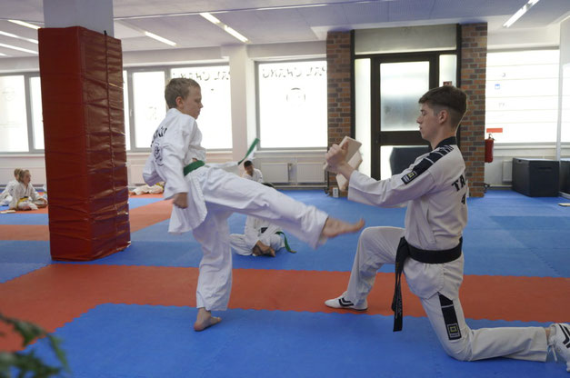 Eine Junge während einer Gürtelprüfung der Kindergruppe im Taekwondo tritt gegen ein Brett.
