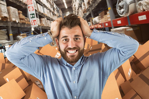 Ein Mann rauft sich die Haare aufgrund zu vieler Pakete in einem Versandlager / Fulfillment-Center