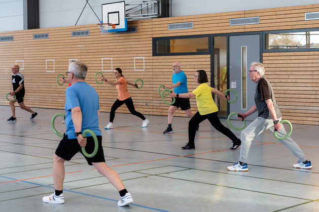 Teilnehmende der Herz- und Rehasportgruppe des BSV Achim führen gemeinsam Kräftigungs- und Koordinationsübungen mit Smovey-Trainingsringen in der Sporthalle durch.