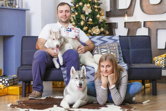 Paar sitz mit zwei Hunden auf einem Sofa und guckt in die Kamera