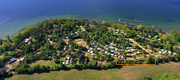 Die Blockhäuser stehen am Rande des Campingplatzes mit Blick auf eine große Wiese und zwischen zwei Seen. © Naturcamping Zwei Seen am Plauer See/MV