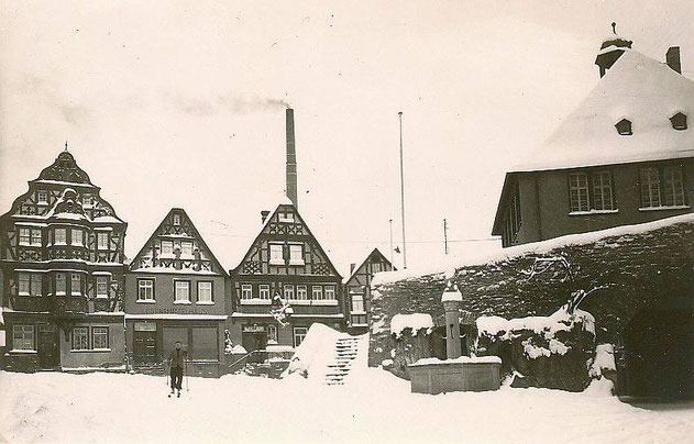 Der verschneite König-Adolf Platz. Im Hintergrund raucht der Schornstein der Fabrik Landauer auf dem heutigen Löherplatz.