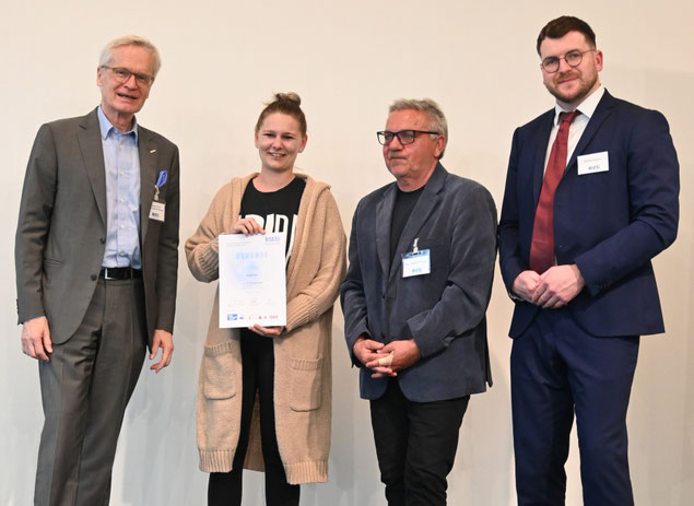 Teilnehmerin präsentiert stolz ihre Urkunde im Beisein der Gratulanten des FAV OÖ