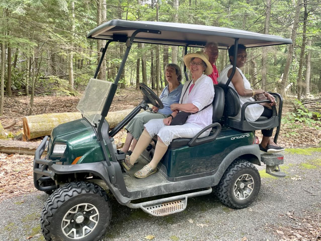 A woman living with cerebral palsy is shown riding in a ClubCar Onward electric golf cart, along with a friend and her caregivers.  