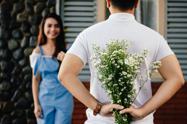 A person hiding a bunch of flowers behind their back.