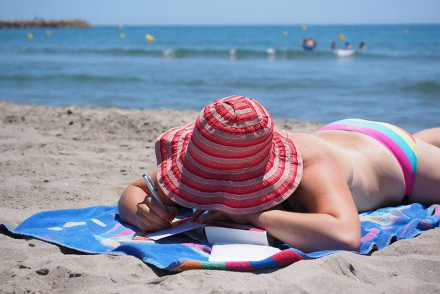 Frau im bunten Bikini mit rotem Sonnenhut liegt am Ostseestrand im Urlaub.