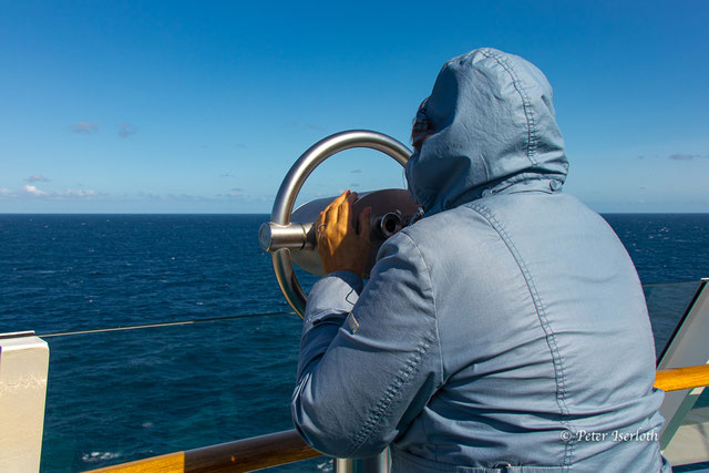 Ein Mensch an einem Fernglas hält "Ausschau", aber außer Weite und Wasser ist nichts zu sehen, außer der Weite des Atlantiks.