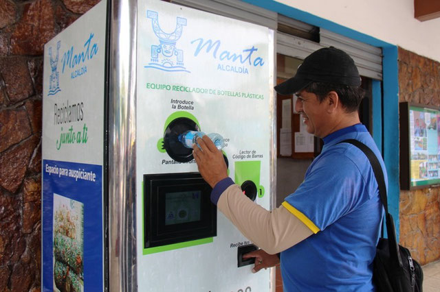 Un usuario introduce una botella plástica en la máquina trituradora instalada al pie del palacio municipal. Manta, Ecuador.