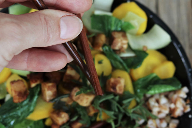 Pak Choi mit Karotten und Tofu werden mit Essstäbchen gegessen