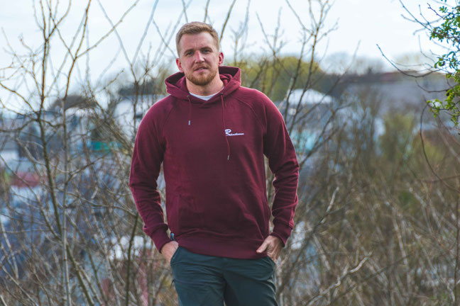 Model trägt nachhaltigen Hoodie mit ‚Rhoihesse‘-Stick auf der Brust – faire, regionale Kleidung aus Rheinhessen in natürlicher Umgebung.