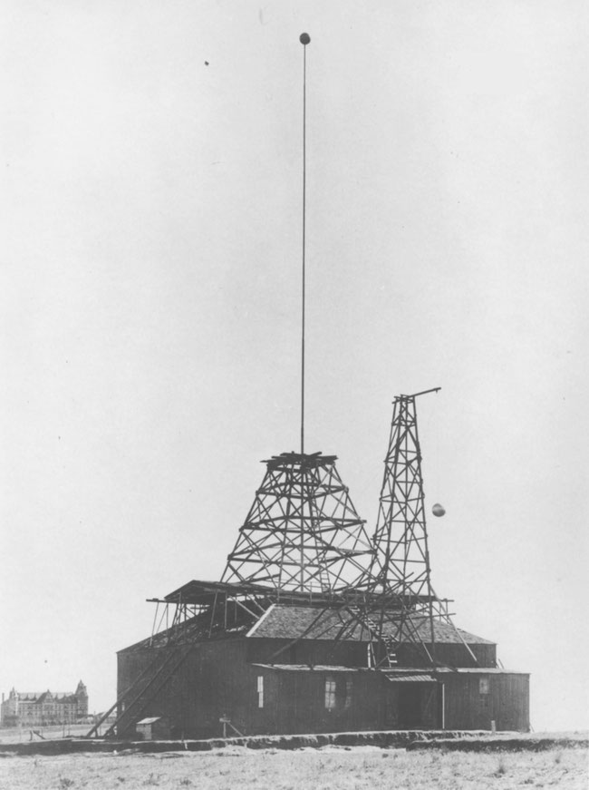 Front view of the Colorado Springs experimental station, with Union Printers Home in background. A special coil wound for investigation of the influence of elevation upon the capacity of an elevated conductor is visible in front of the laboratory. 1899 