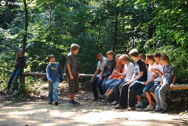 Jugendliche sitzen im Wald auf einem Baumstamm. Bild von Ortrun Lenz auf Pixabay.