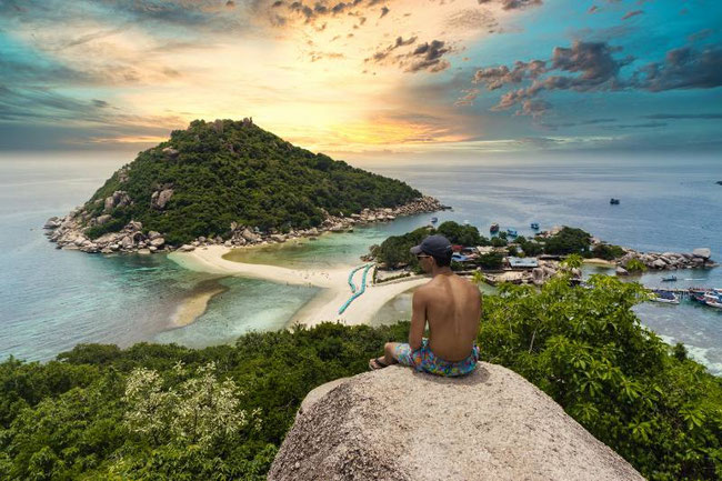 A man sitting on a rock with an Island in the background