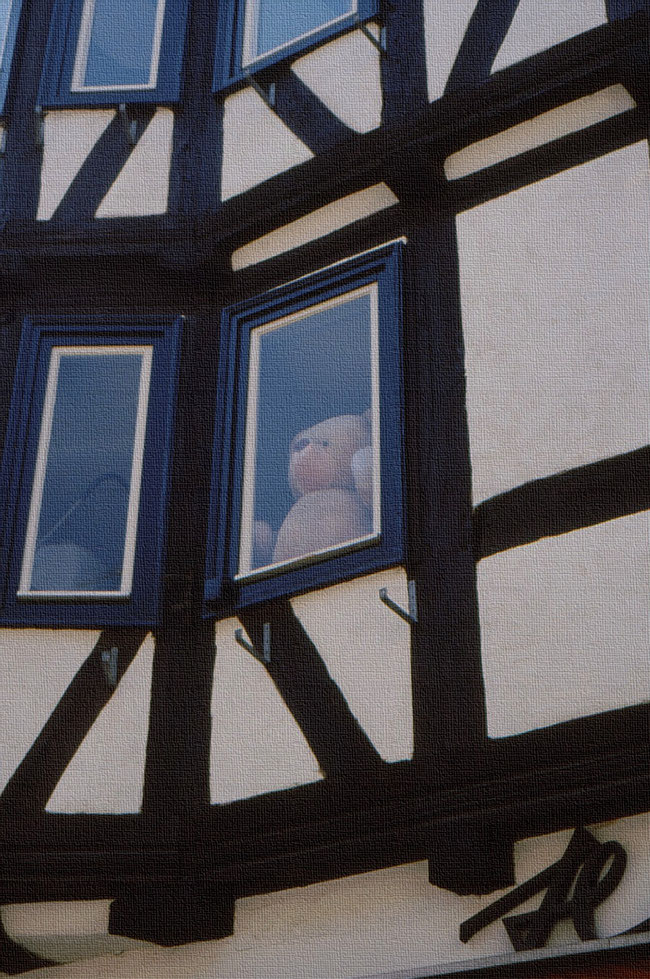 Teddybär winkt am Fenster eines Fachwerkhauses