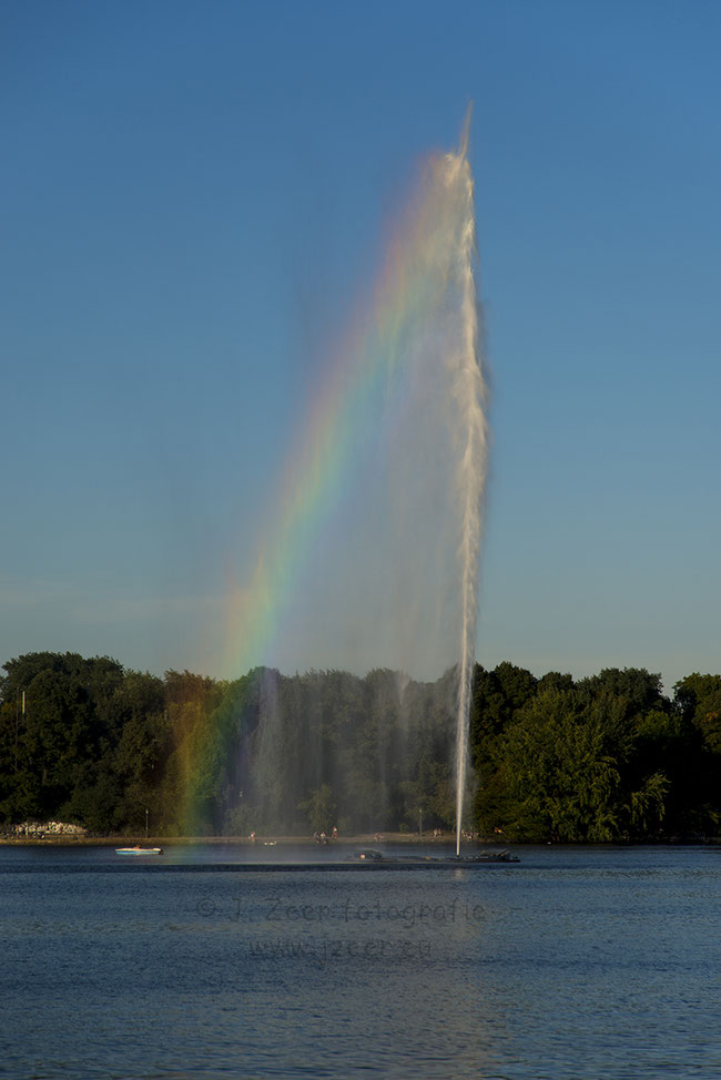 Deze fontein ligt op de Binnenalster in het centrum van Hamburg. Door een combinatie van mooie blauwe lucht, een klein briesje en laag staande zon komt deze regenboog tevoorschijn.