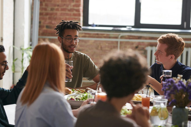 Een groep mensen aan tafel die eten en een goed gesprek hebben