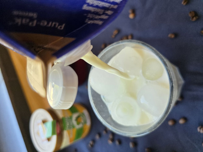 Kalte Milch über die Eiswürfel im Glas gießen für Iced Honey Latte