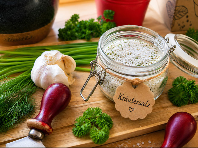 Selbstgemachtes Kräutersalz im Mörser mit frischen Kräutern, Knoblauch und Wiegemesser auf rustikalem Holzbrett – einfaches DIY-Rezept von Mummys Taste. 