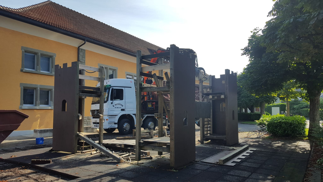 Ein weisser Lastwagen von Gerster Recycling steht bei Demontage- und Abbrucharbeiten. Im Hintergrund sind mehrere grosse rote Abfallcontainer mit dem Logo von Gerster Recycling zu sehen. Das Bild zeigt einen Recycling- und Abfallentsorgungsbetrieb.