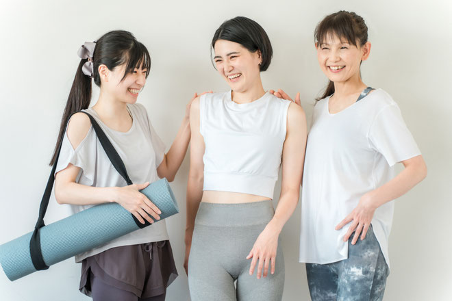 ピラティスのレッスン後に談笑する3人の女性。幅広い年代の参加者がウエア姿で笑顔を見せる、アットホームなスタジオです。