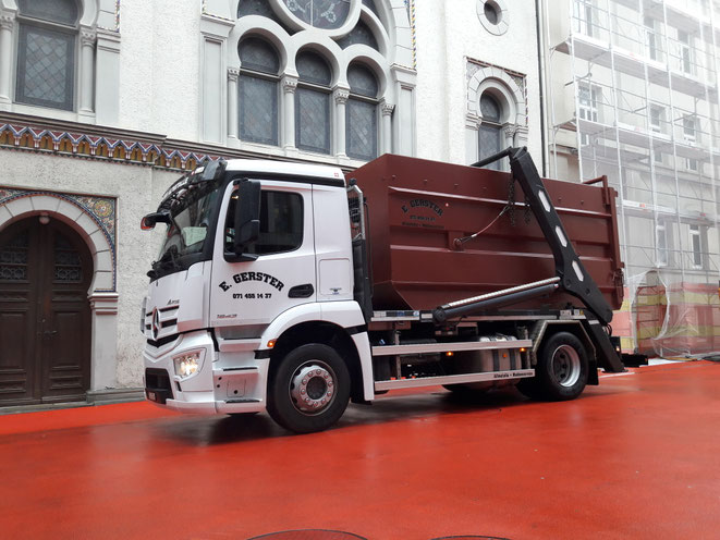 Ein weisser Lastwagen von Gerster Recycling steht am Abbruch und der Demontage eines Wohnwagens. Es ist ein Kran mit Greifer und Logo von Gerster Recycling zu sehen. Das Bild zeigt einen Transport und Muldenservice.