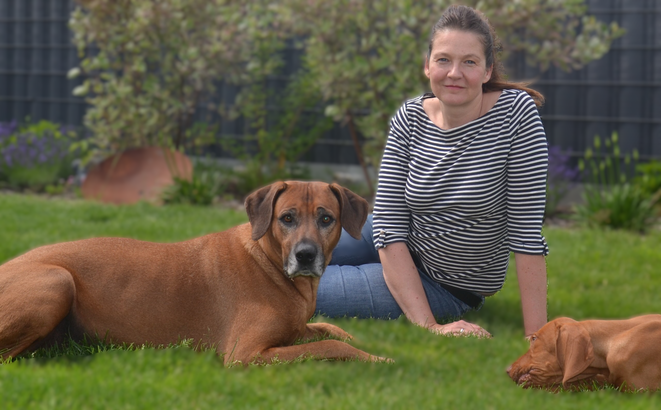 das Bild zeigt die Hundetrainerin und Verhaltensberaterin Daniela Seemann mit ihren Hunden Bruno und Stuart auf einem rasen im Garten sitzend nach einem Hundetraining im Jahr 2025