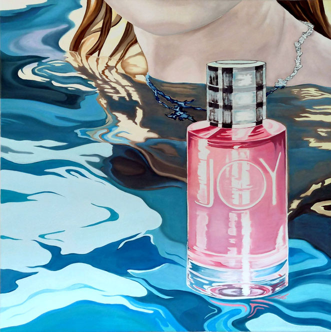 Eine rosafarbene Parfümflasche im Vordergrund und eine Teilansicht einer blonden Frau sind verbunden durch eine Wasserfläche mit Spiegelung 