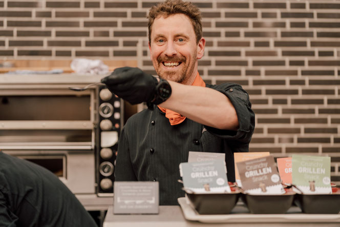 Fröhlich lächelnd bietet der Koch etwas zu Probieren an.