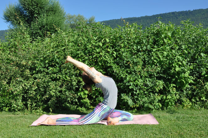 Eine Yogaübung auf einer Yogamatte im Freien auf einer Grasfläche und vor Büschen