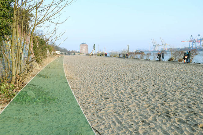 Der leere Strand in Övelgönne an einem sonnigen Wintertag, einige Menschen flanieren auf dem Betonweg neben den Schlackesteinen