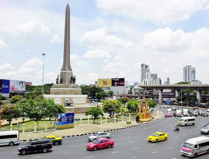 タイ王国・首都バンコク「ビクトリーモニュメント/ Victory Monument Station(BTS)」 駅前の光景。戦勝記念塔が写真奥に、写真手前には道路。車、タクシーなどが走る