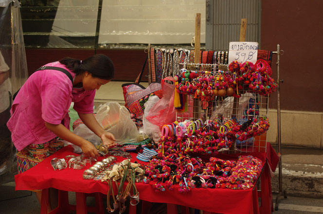 タイの少数民族 モン族？の手製アクセサリー、雑貨小物などを扱うお店。販売光景。店員の女性が仕事をしている。チェンマイ サタデーマーケット[タイ・チェンマイ旅行（出張）写真ブログの画像]