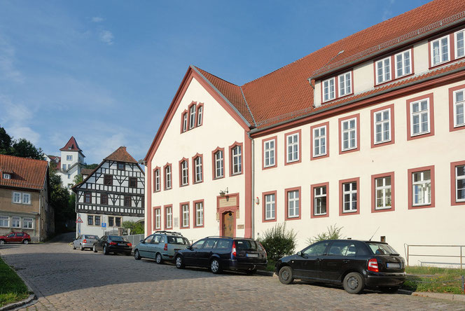 Eine komplette Vorderansicht des Martin-Luther-Gymnasiums in Eisenach. Davor parken fünf Pkw. Links hinten sieht man ein Fachwerkhaus und eine Art Turm.