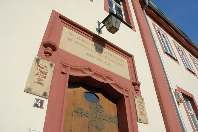 Man blickt fast senkrecht am Martin-Luther-Gymnasium an der historischen Holz-Eingangstüre nach oben. Links und rechts sind zwei Gedenktafeln, rechts sieht man Fenster. 