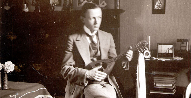 Auch er ist ein Mitglied der Bach-Familie: Herbert Bach sitzt mit einer Mandoline in einem früheren Wohnraum. Er hat ein Jacket und eine Krawatte an und schaut nach links. Das Foto ist schwarzweiß.
