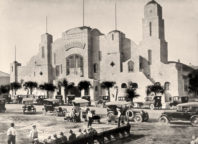 Downtown St. Petersburg, Florida in den USA. Es ist ein historisches, schwarzweißes Foto. Im Vordergrund sind viele historische Oldtimer und viele Menschen.