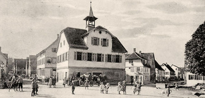 Die Ortsmitte von Flein bei Heilbronn auf einem historischen Foto. Viele Menschen sieht man vor dem Alten Rathaus. Das Motiv ist schwarzweiß. Man sieht in zwei Straßenzüge rechts und links.