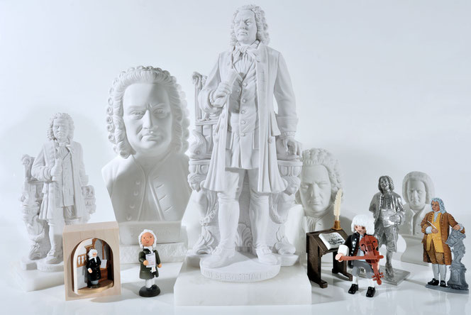 Around 15 Bach figures stand against a white background: gypsum statues, gypsum busts in various sizes, Erzgebirge (Ore Mountains) wooden figures, the Little Bach Figure and Bach tin figures.